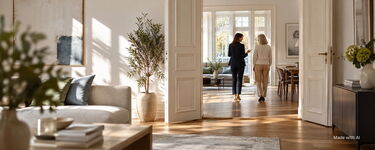 Eine Eigentümerin geht mit einer Maklerin durch ihre helle und modernisierte Altbau-Wohnung